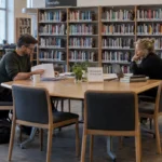 Two adults review comparison criteria together at a library table while assessing Swedish-licensed casinos.